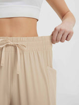 Close-up on beige women's running sweatpants elastic waistband with drawstring and pocket. #color_Khaki