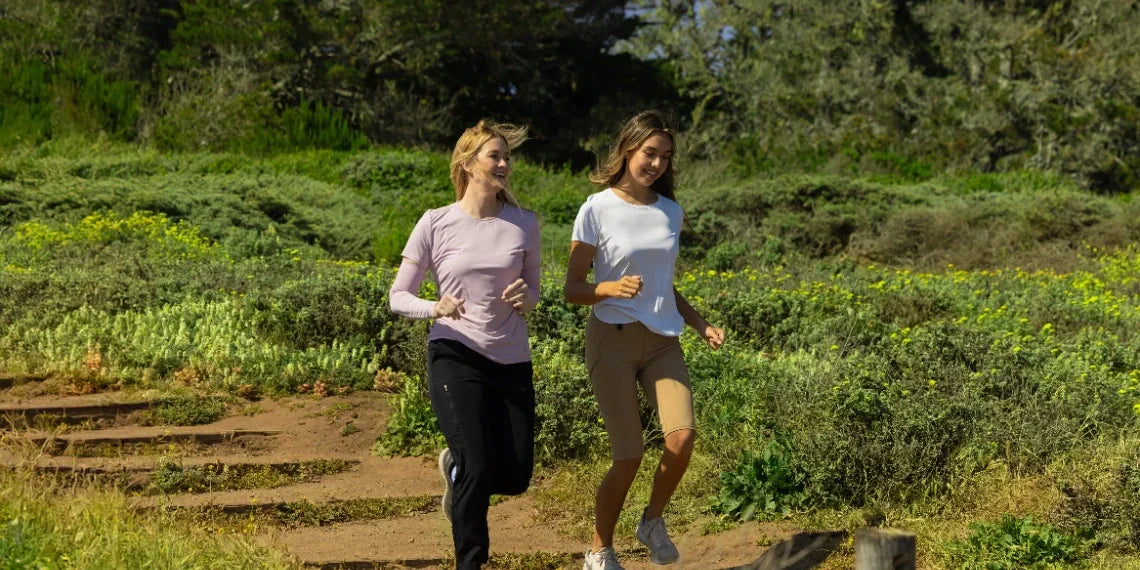 Two women jogging outdoors in pink and white tops with black pants and tan biker shorts