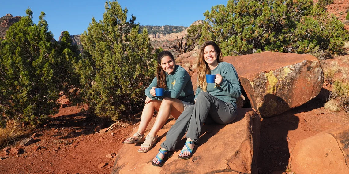 Two women relaxing on red rocks with mugs outdoors