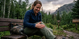 Woman hiker checking water beading on green hiking pants beside a mountain trail