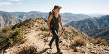 Woman hiker in dark hiking pants walking with trekking poles on a rocky mountain trail