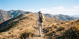 Woman hiker with backpack and trekking poles walking along a mountain trail