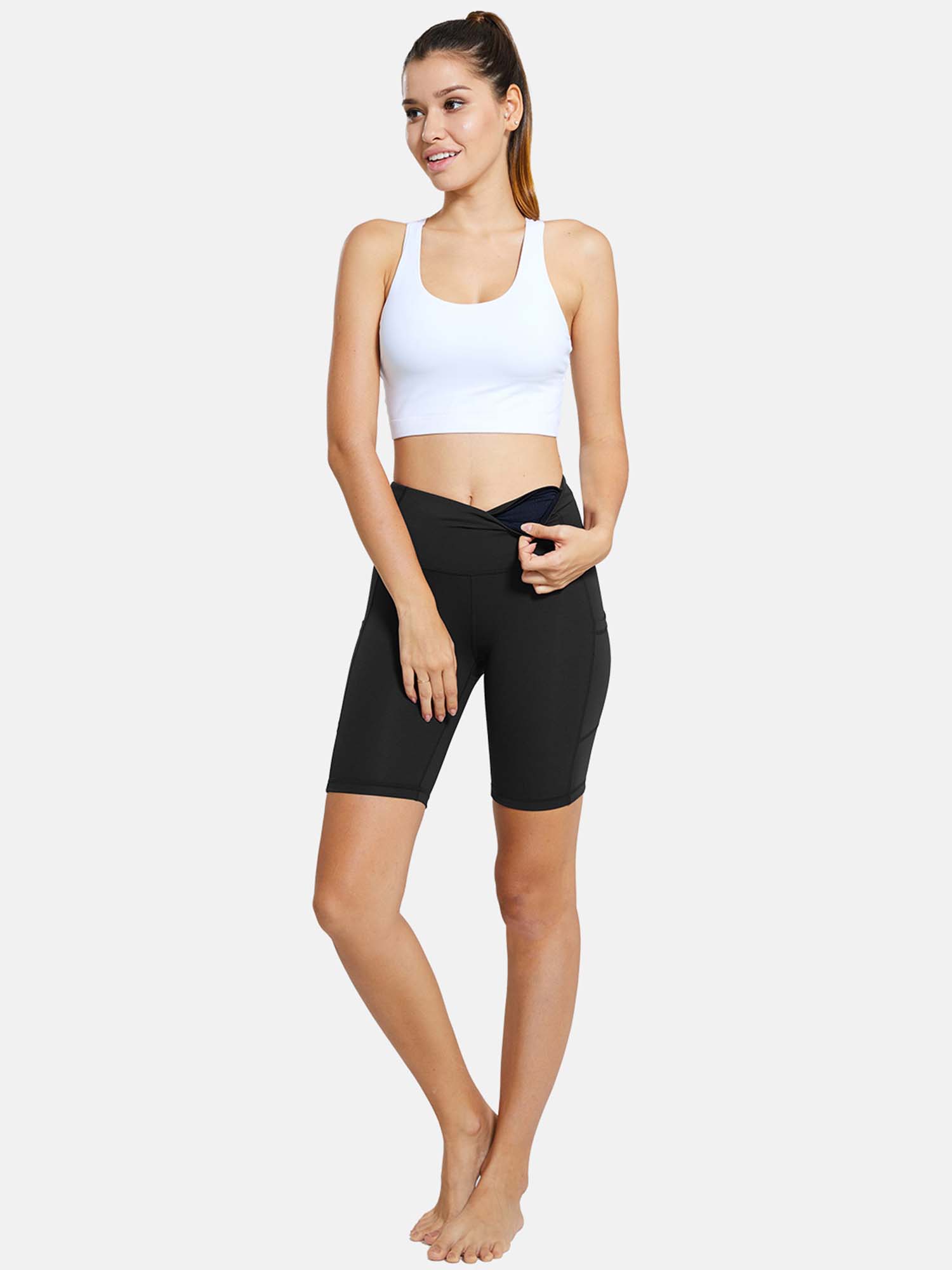 Black 7" high waist yoga shorts with pockets on a woman, paired with a white sports bra. #color_Black
