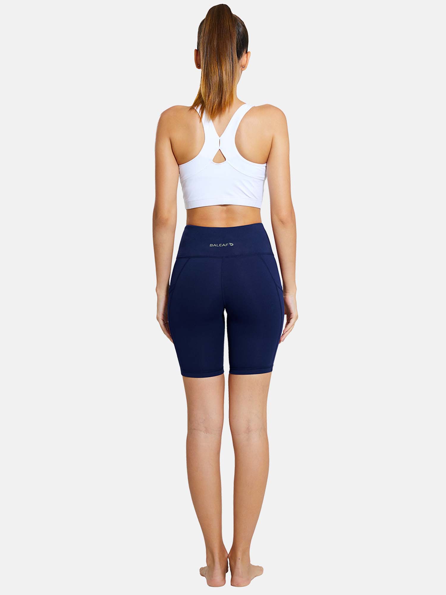 Navy blue Baleaf 7" yoga shorts with pockets, back view. Paired with white sports bra.