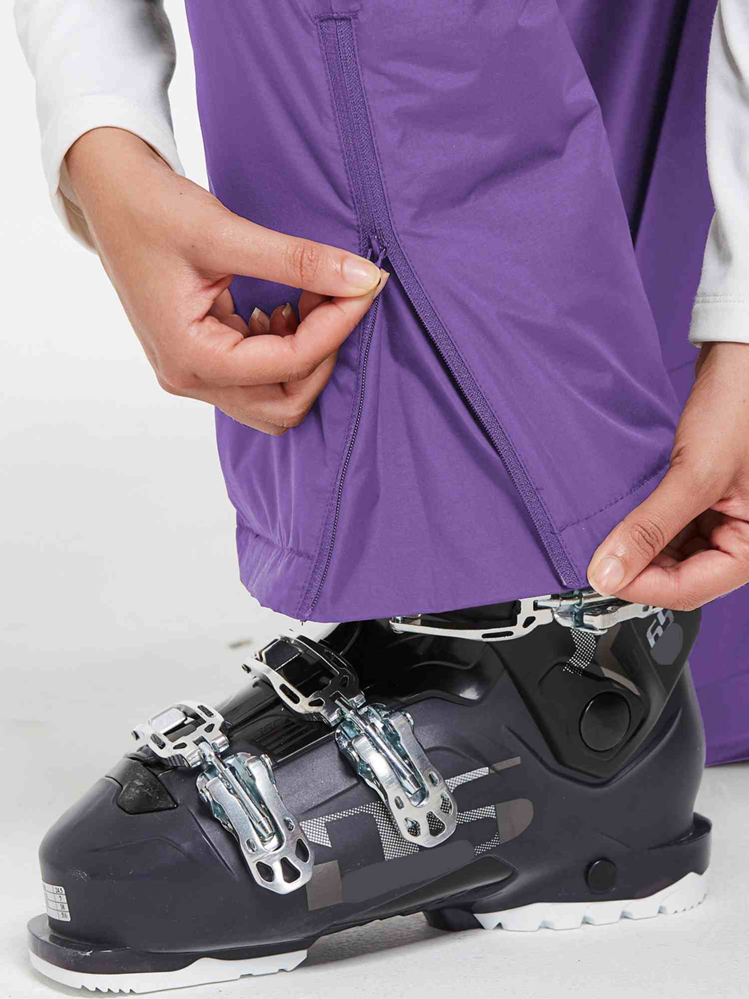 Outdoor ski bib pants in purple, showing zipper detail with ski boot #color_Purple