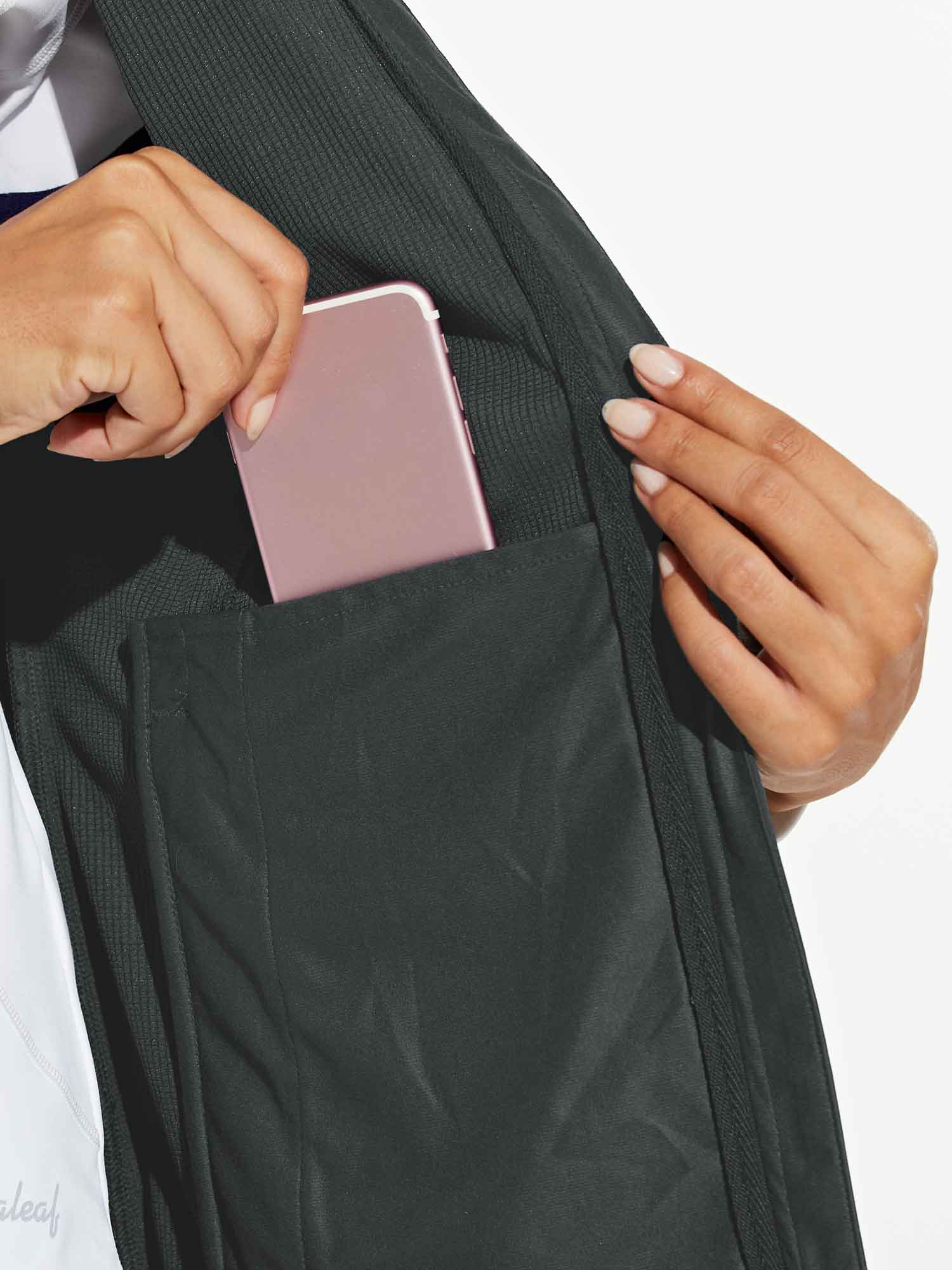 Woman places rose gold smartphone in dark gray windproof softshell vest zippered pocket. Practical storage for active women.