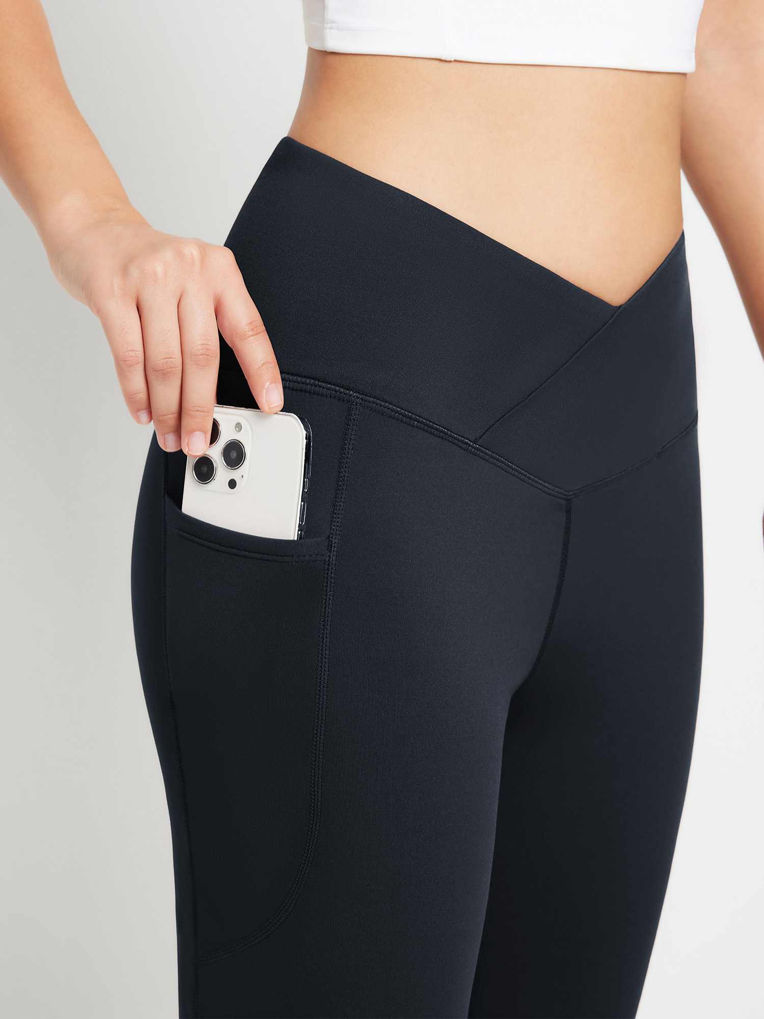 Black crossover waist yoga flare pants with pocket holding phone. #color_Black