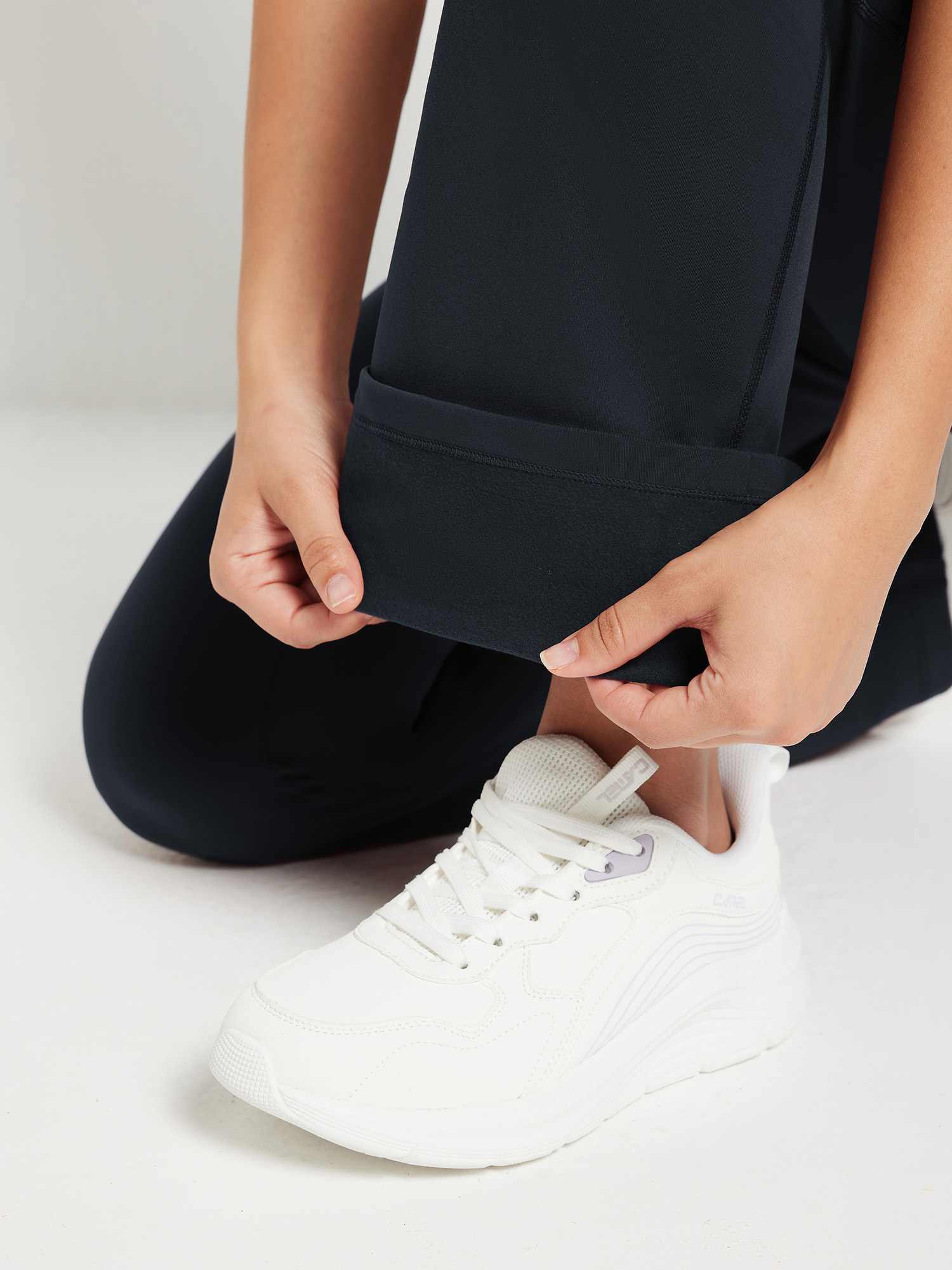 Black fleece yoga flare pants detail: soft lining visible as hem is folded, white sneaker. #color_Black