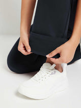 Black fleece yoga flare pants detail: soft lining visible as hem is folded, white sneaker. #color_Black
