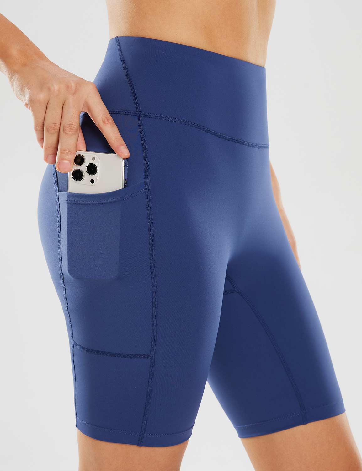 Blue women's 8" yoga shorts with side pockets holding a phone.