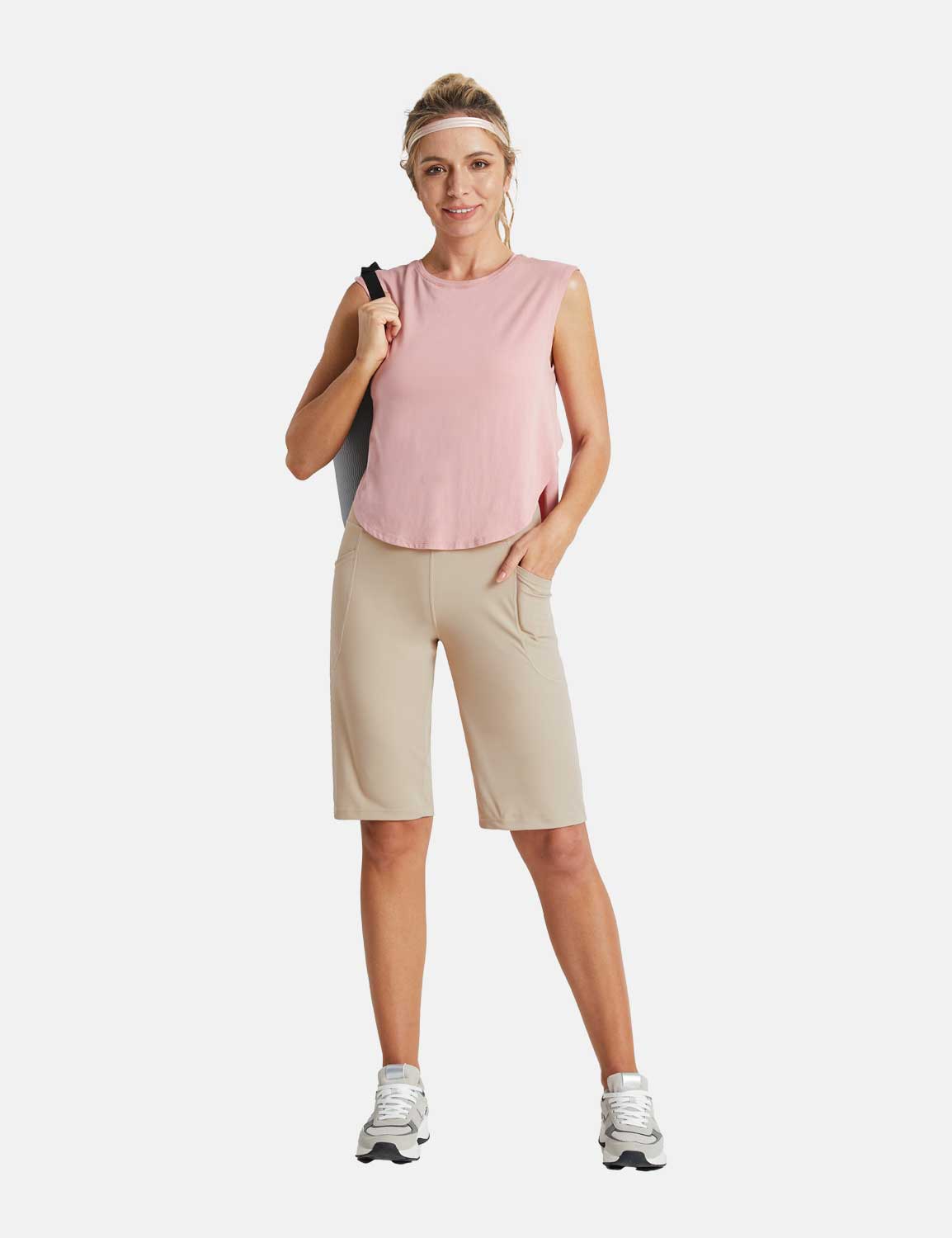 Woman wearing a pink sleeveless top and khaki 12-inch inseam running shorts, carrying a yoga mat.